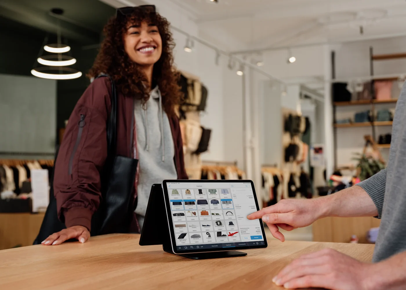 Agence Shopify : une cliente et un commerçant devant une caisse sur tablette affichant le catalogue d’une boutique de vêtements